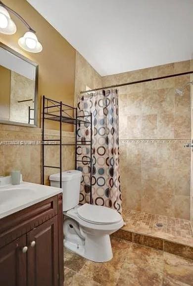 bathroom with a shower with shower curtain, vanity, toilet, and tile walls