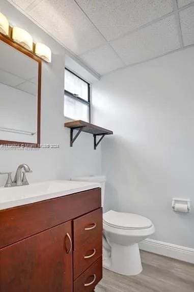 bathroom with hardwood / wood-style floors, vanity, a drop ceiling, and toilet