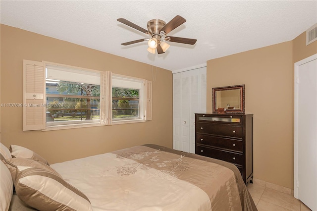 bedroom with ceiling fan, a closet, light tile patterned floors, and a textured ceiling