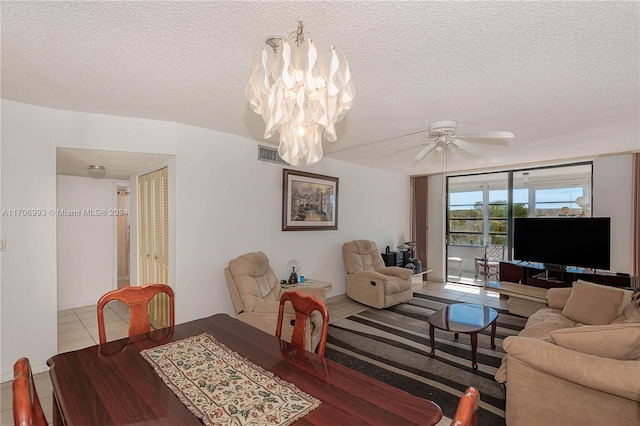 tiled dining space with ceiling fan with notable chandelier and a textured ceiling