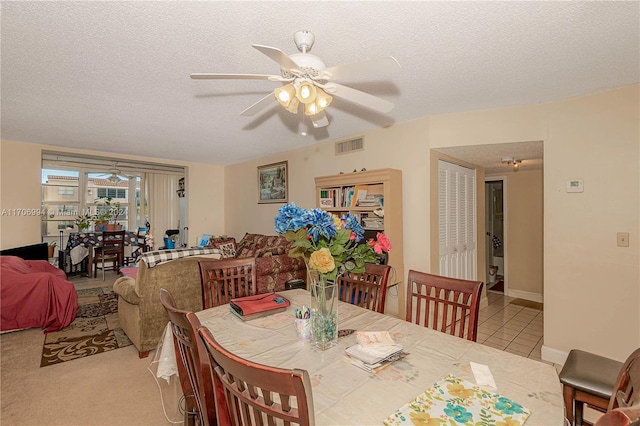 dining room featuring ceiling fan, light colored carpet, and a textured ceiling