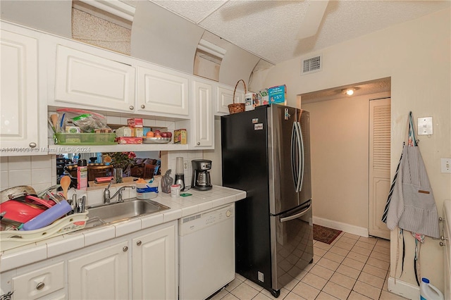 kitchen featuring white dishwasher, tile counters, white cabinetry, and stainless steel refrigerator