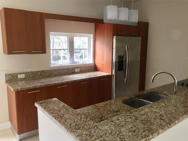 kitchen with decorative light fixtures, stainless steel fridge, light stone countertops, and sink