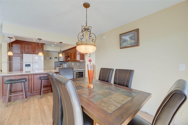 dining room with a chandelier, a textured ceiling, light hardwood / wood-style floors, and wine cooler