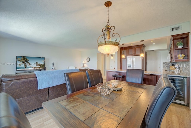 dining space featuring a textured ceiling, visible vents, wine cooler, and light wood-style floors
