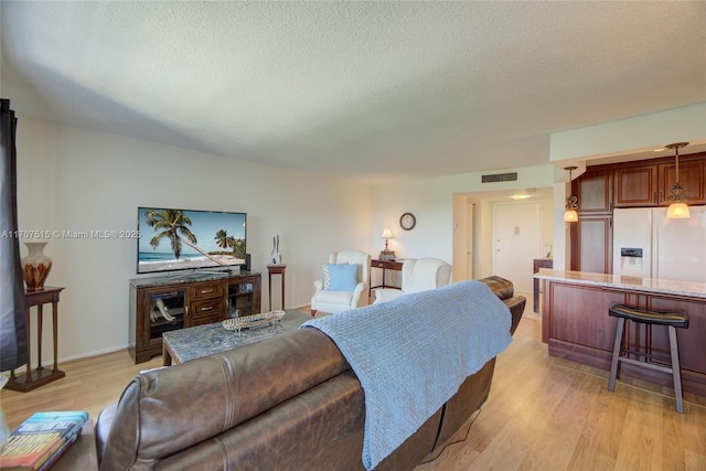 living room with a textured ceiling, baseboards, light wood finished floors, and visible vents
