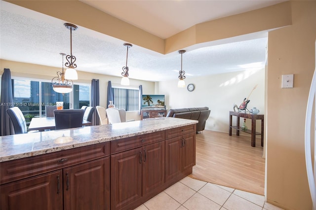 kitchen featuring hanging light fixtures, light hardwood / wood-style flooring, a textured ceiling, dark brown cabinets, and light stone counters