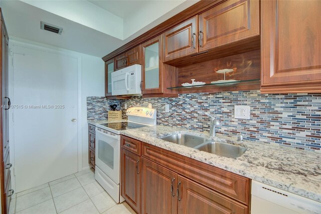 kitchen with a sink, light stone countertops, light tile patterned floors, white appliances, and decorative backsplash