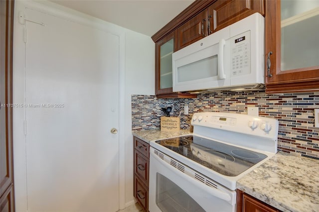 kitchen with decorative backsplash, glass insert cabinets, light stone countertops, and white appliances