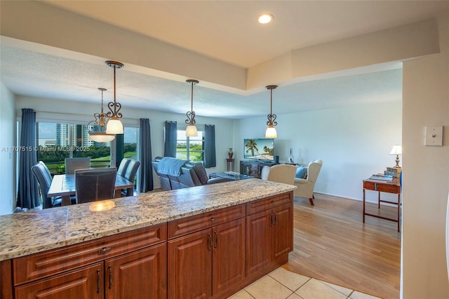 kitchen with light tile patterned flooring, light stone countertops, decorative light fixtures, and brown cabinetry