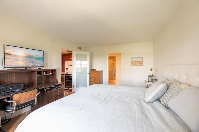bedroom with wine cooler, connected bathroom, visible vents, white fridge with ice dispenser, and wood finished floors