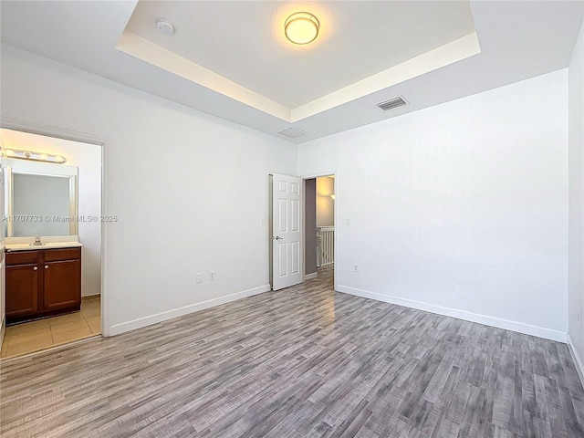 unfurnished bedroom featuring connected bathroom, sink, light hardwood / wood-style flooring, and a tray ceiling