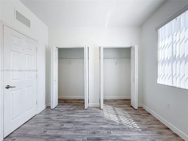 unfurnished bedroom featuring wood-type flooring and two closets