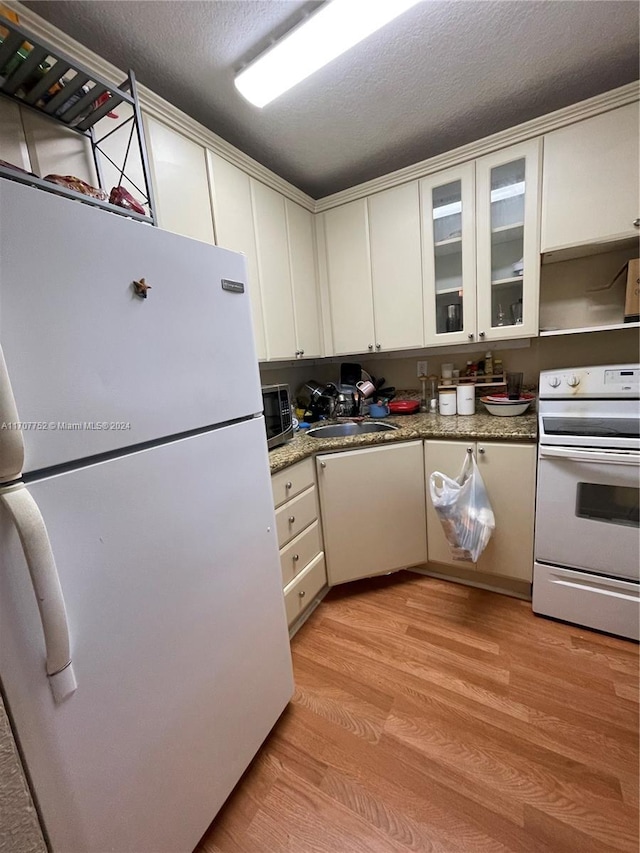 kitchen with white appliances, white cabinets, sink, light wood-type flooring, and a textured ceiling