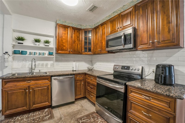 kitchen featuring sink, decorative backsplash, dark stone countertops, a textured ceiling, and stainless steel appliances