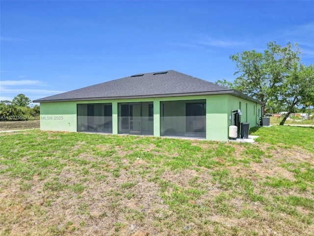 back of property with a sunroom, stucco siding, roof with shingles, central AC, and a lawn