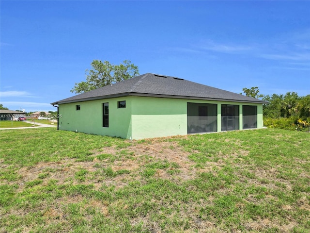rear view of house with a sunroom, stucco siding, a yard, and a shingled roof