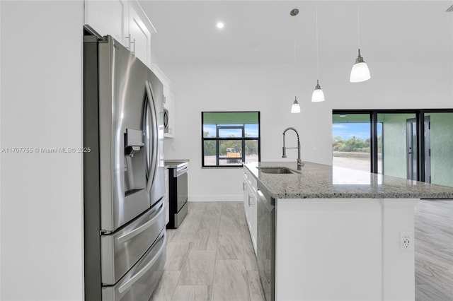 kitchen featuring white cabinetry, hanging light fixtures, a sink, a kitchen island with sink, and appliances with stainless steel finishes