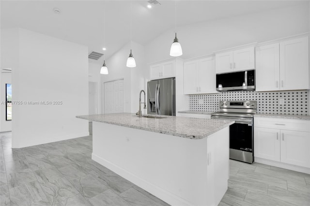 kitchen featuring decorative backsplash, an island with sink, white cabinets, light stone countertops, and appliances with stainless steel finishes