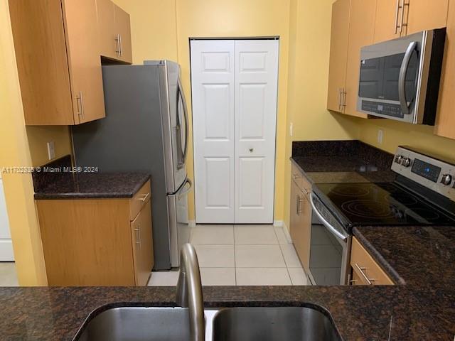 kitchen featuring light tile patterned flooring, sink, stainless steel appliances, and dark stone counters