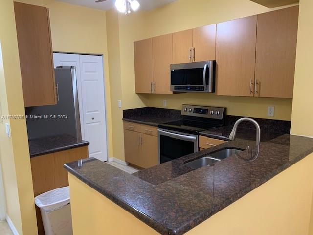 kitchen featuring kitchen peninsula, stainless steel appliances, ceiling fan, sink, and dark stone countertops