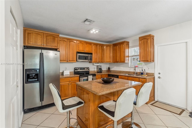 kitchen with sink, stainless steel appliances, light tile patterned floors, a kitchen breakfast bar, and a kitchen island