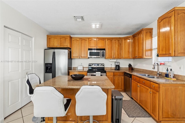 kitchen with appliances with stainless steel finishes, sink, light tile patterned floors, a center island, and a breakfast bar area