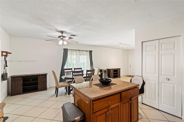 kitchen featuring light tile patterned floors, a textured ceiling, a kitchen island, and ceiling fan