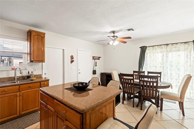 kitchen featuring ceiling fan, sink, a center island, a textured ceiling, and light tile patterned floors