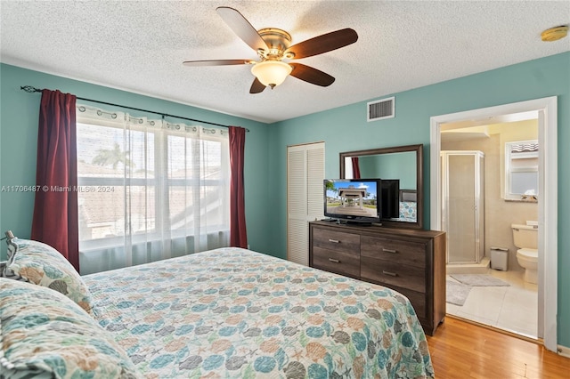 bedroom with ensuite bathroom, light hardwood / wood-style flooring, ceiling fan, a textured ceiling, and a closet