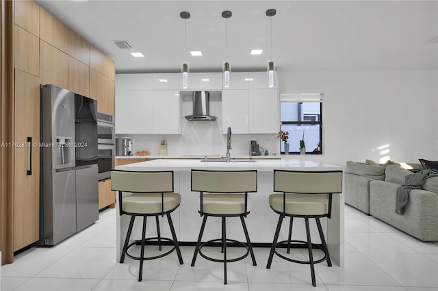 kitchen with white cabinetry, wall chimney range hood, pendant lighting, light tile patterned floors, and appliances with stainless steel finishes