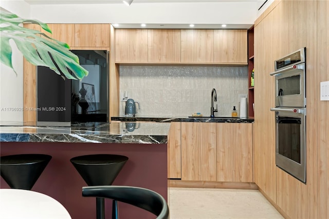 kitchen with dark stone counters, sink, decorative backsplash, light brown cabinetry, and stainless steel double oven