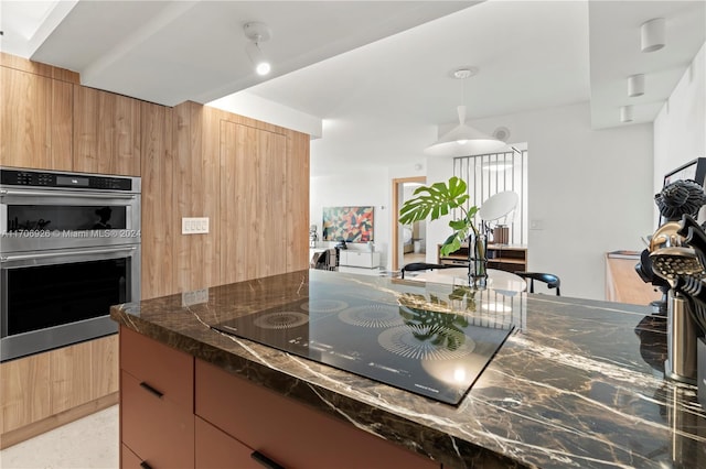 kitchen featuring hanging light fixtures, black electric stovetop, double oven, and dark stone countertops