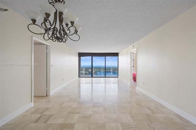 empty room featuring expansive windows, a textured ceiling, and a chandelier