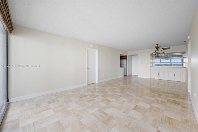 unfurnished room with a chandelier and a textured ceiling