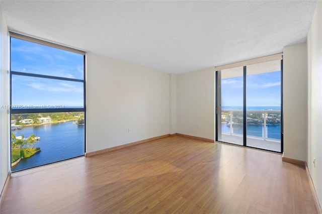 spare room with expansive windows, light hardwood / wood-style flooring, a water view, and a textured ceiling