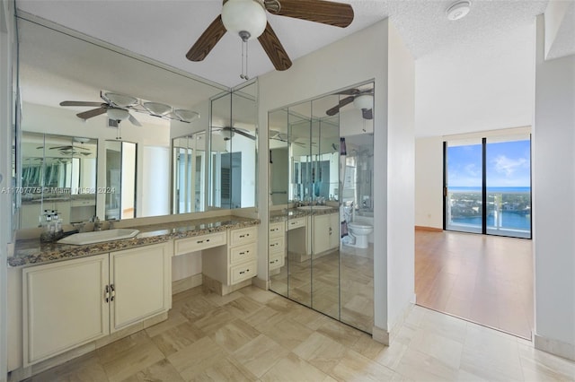 bathroom featuring ceiling fan, a textured ceiling, toilet, a water view, and vanity