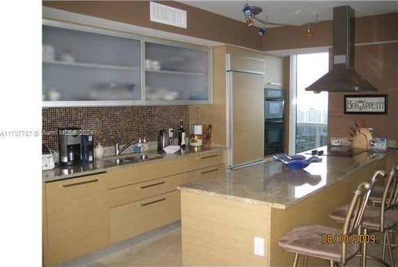 kitchen with sink, island exhaust hood, a kitchen bar, decorative backsplash, and black appliances