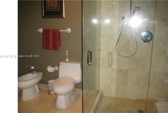 bathroom with tile patterned floors, toilet, a shower with shower door, and a bidet