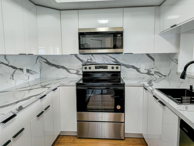 kitchen featuring light stone countertops, appliances with stainless steel finishes, sink, light hardwood / wood-style flooring, and white cabinets