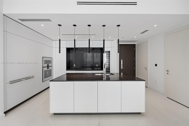 kitchen featuring sink, light tile patterned floors, white cabinetry, hanging light fixtures, and an island with sink