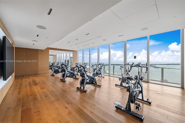 exercise room with light hardwood / wood-style floors, a water view, and a wall of windows