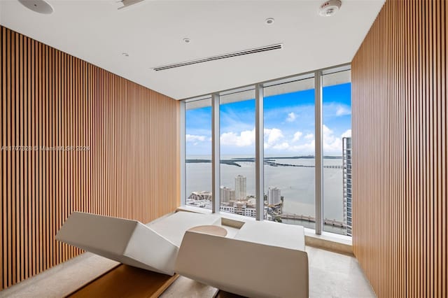 dining space with a water view, a wall of windows, and wooden walls