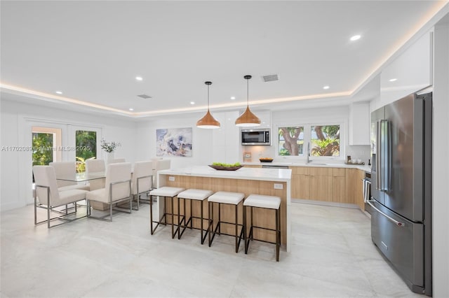 kitchen featuring appliances with stainless steel finishes, a tray ceiling, hanging light fixtures, and a center island