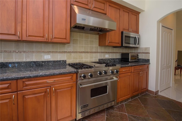 kitchen with dark stone countertops, appliances with stainless steel finishes, tasteful backsplash, and exhaust hood