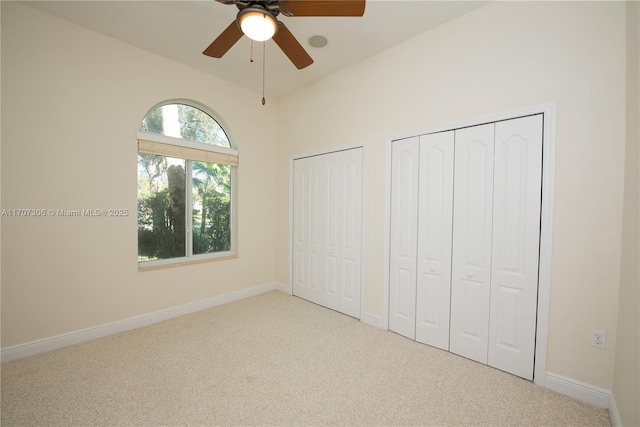 unfurnished bedroom with ceiling fan, vaulted ceiling, light carpet, and two closets