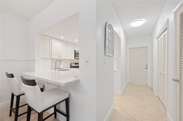 kitchen featuring a kitchen breakfast bar, sink, kitchen peninsula, a textured ceiling, and white cabinetry