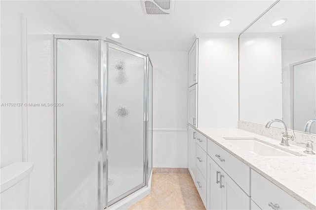 bathroom featuring tile patterned flooring, vanity, a shower with shower door, and toilet