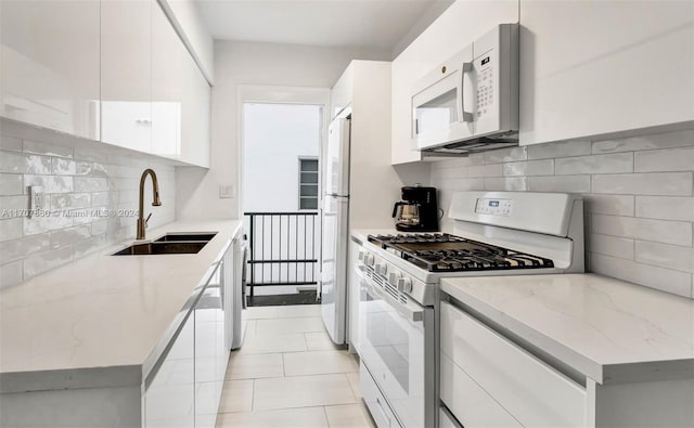 kitchen with white cabinetry, sink, light stone counters, white appliances, and light tile patterned flooring