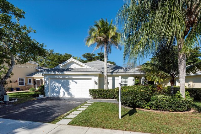 ranch-style house featuring driveway, an attached garage, a front lawn, and stucco siding